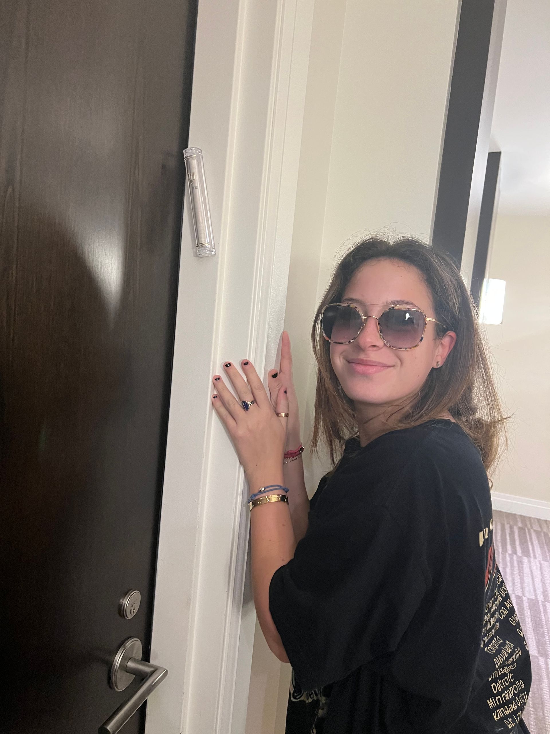 A woman wearing sunglasses is leaning against a door.