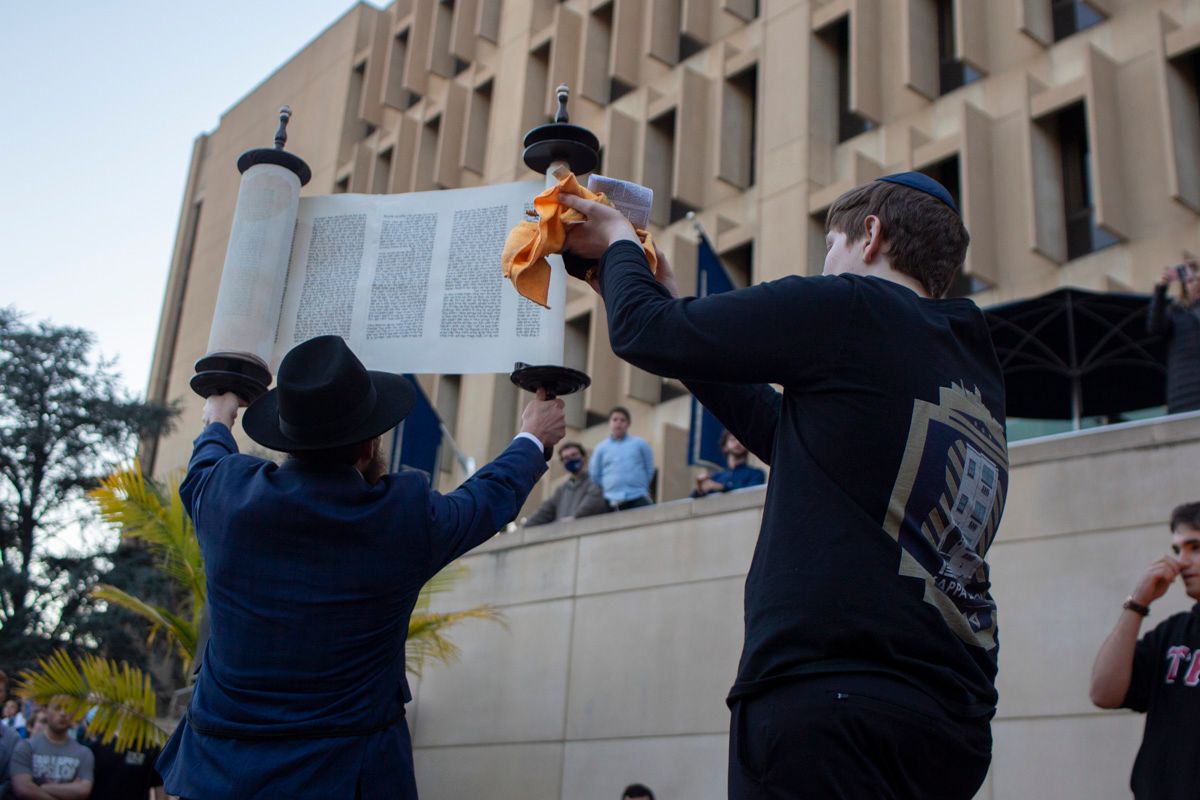 Two men are holding a torah scroll in front of a building.
