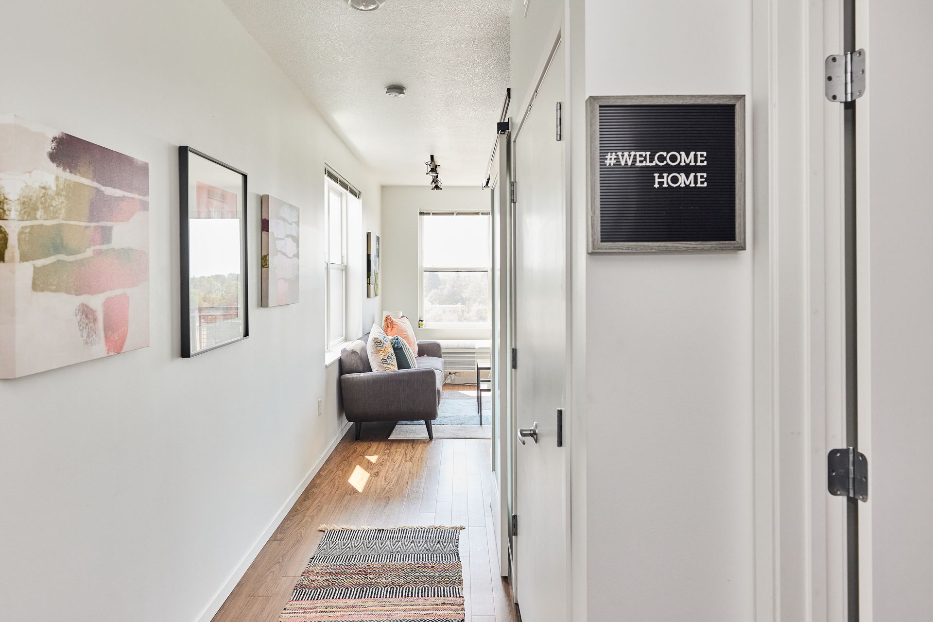 Long hallway with art, rug, and door to living room. Sign reads 