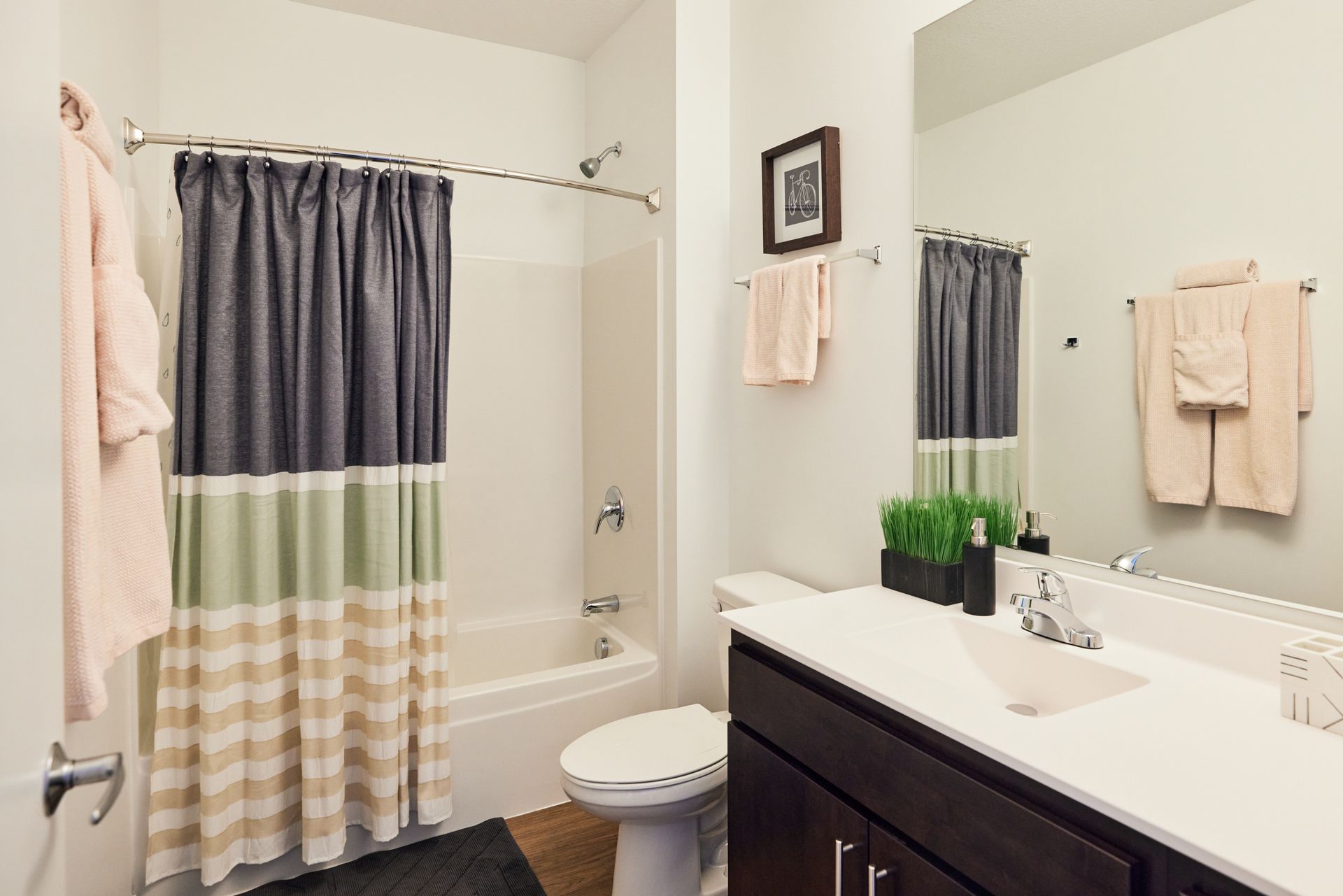 Bathroom with dark brown vanity, white countertop, shower with patterned curtain, and mirror.