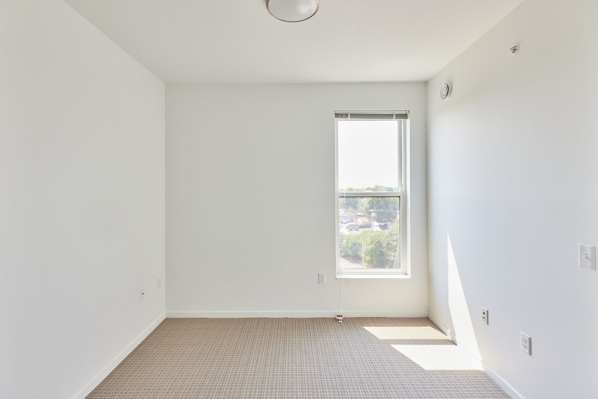 Empty room with beige carpet, a small window, and white walls.