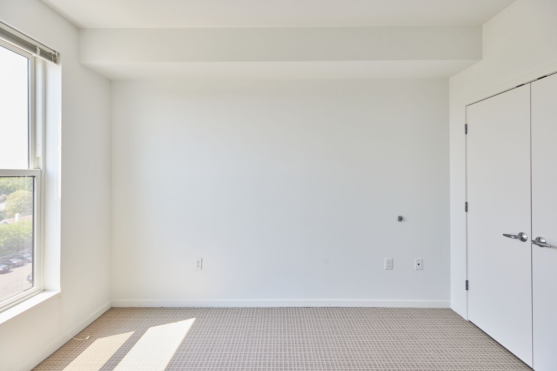 Empty white room with a window, door, and light-colored carpet.