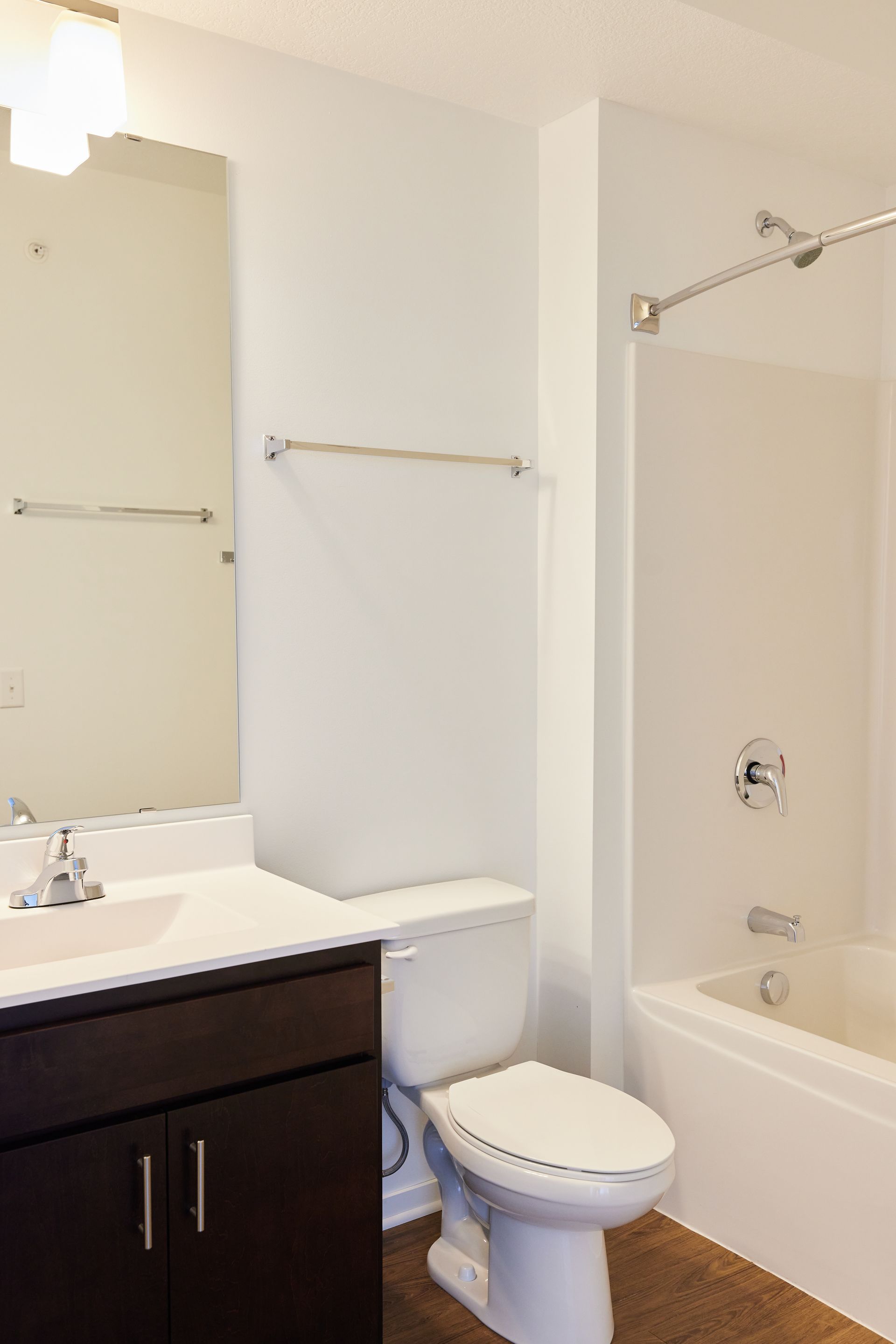 Bathroom with a toilet, sink, mirror, and bathtub. White walls and a dark brown cabinet.