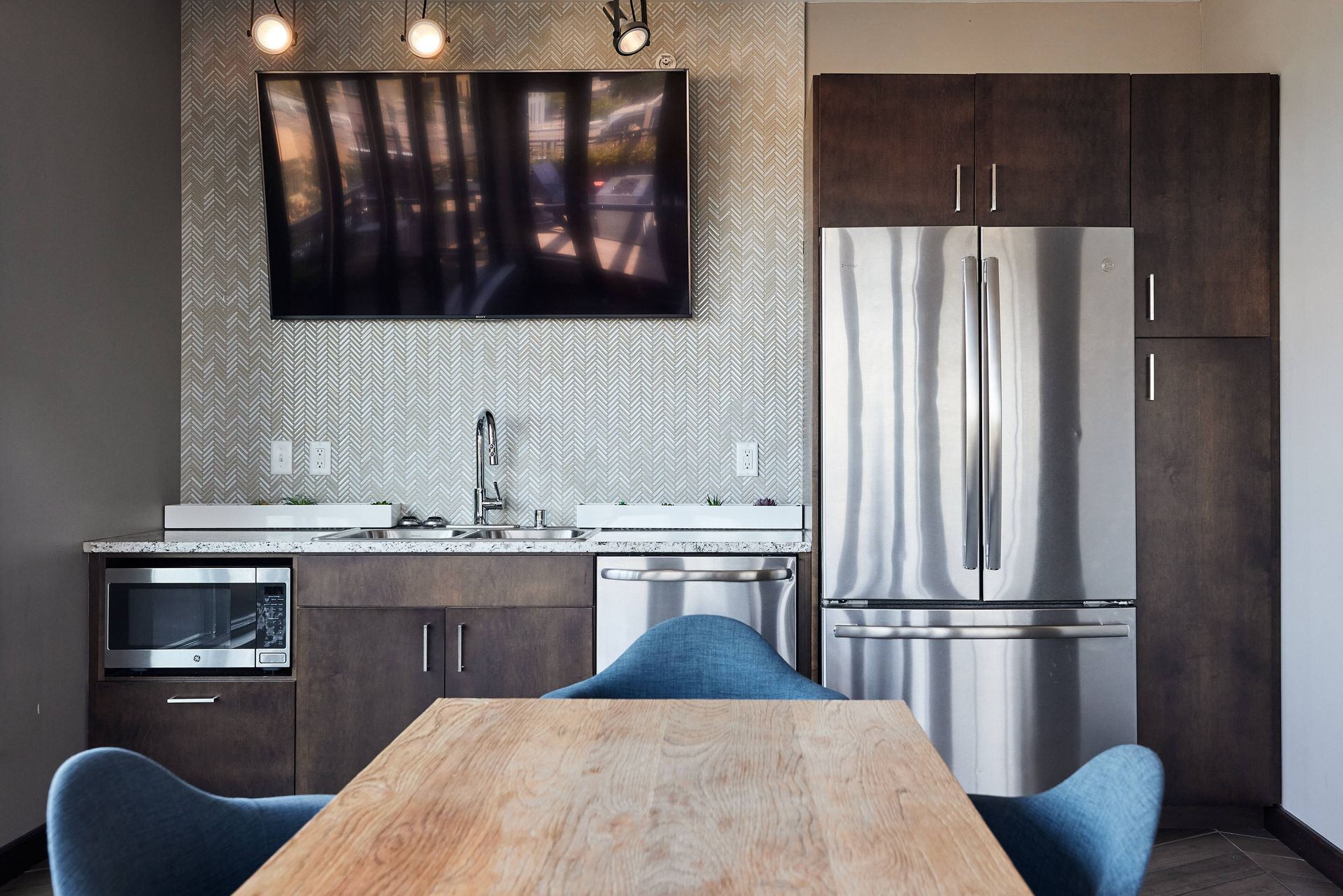 Kitchen area with wooden table, stainless steel appliances, and television on textured wall at Southsider Apartments in Minneapolis, MN.