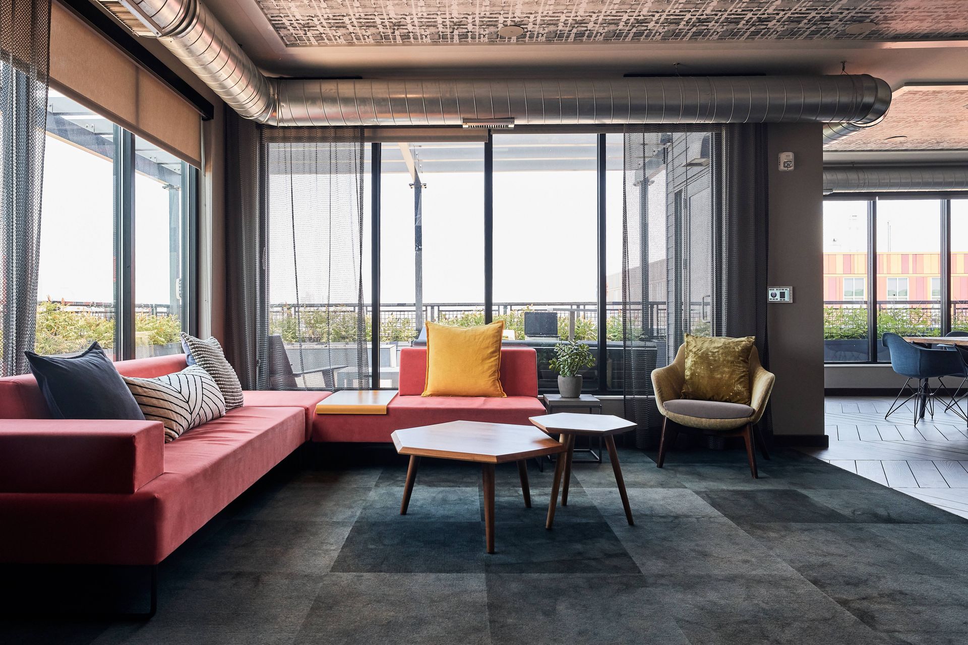 Modern office lounge with pink sofa, coffee tables, and city view through large windows.