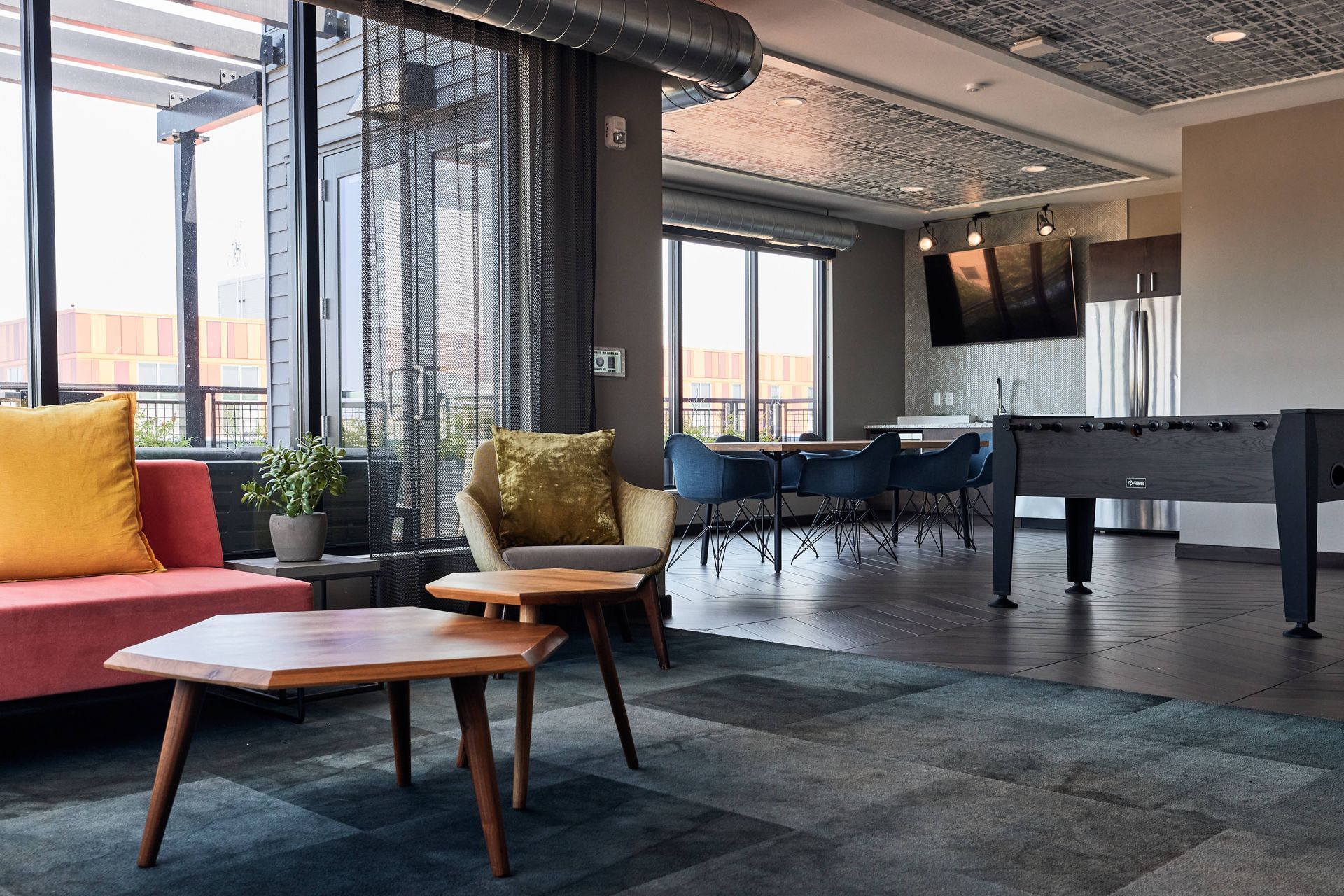 Modern lounge area with seating, foosball, kitchen, and large windows.