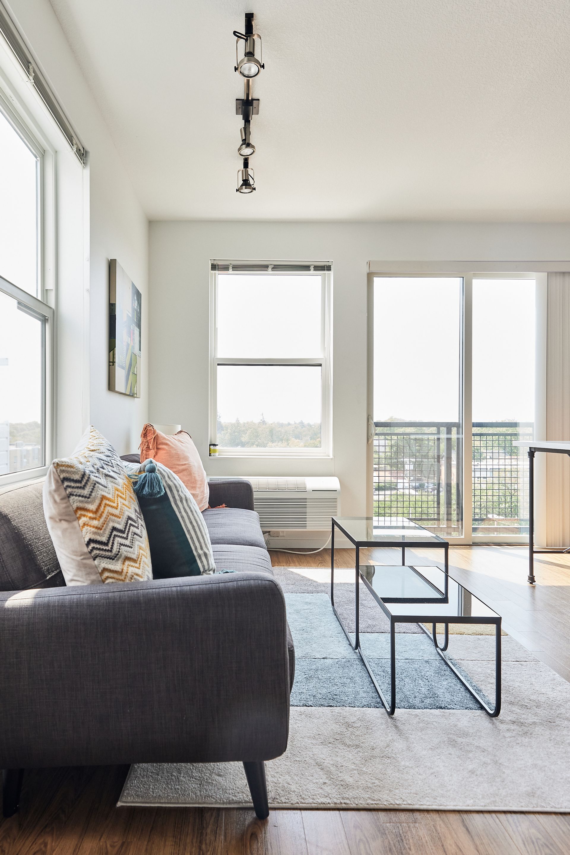 Living room with a gray couch, windows, and a sliding glass door leading to a balcony at Southsider Apartments in Minneapolis, MN.
