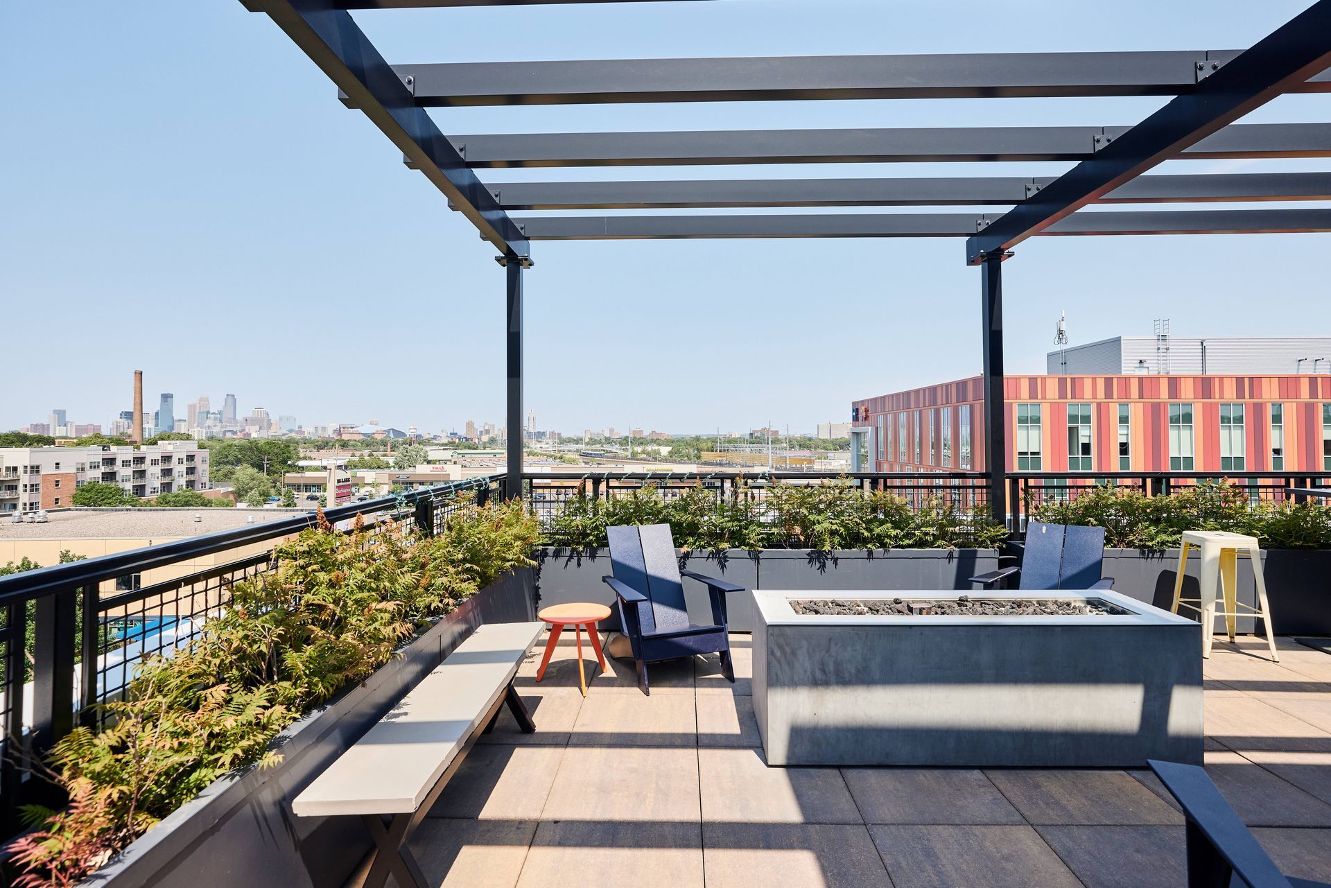 Rooftop patio with seating, a fire pit, and city view on a sunny day.