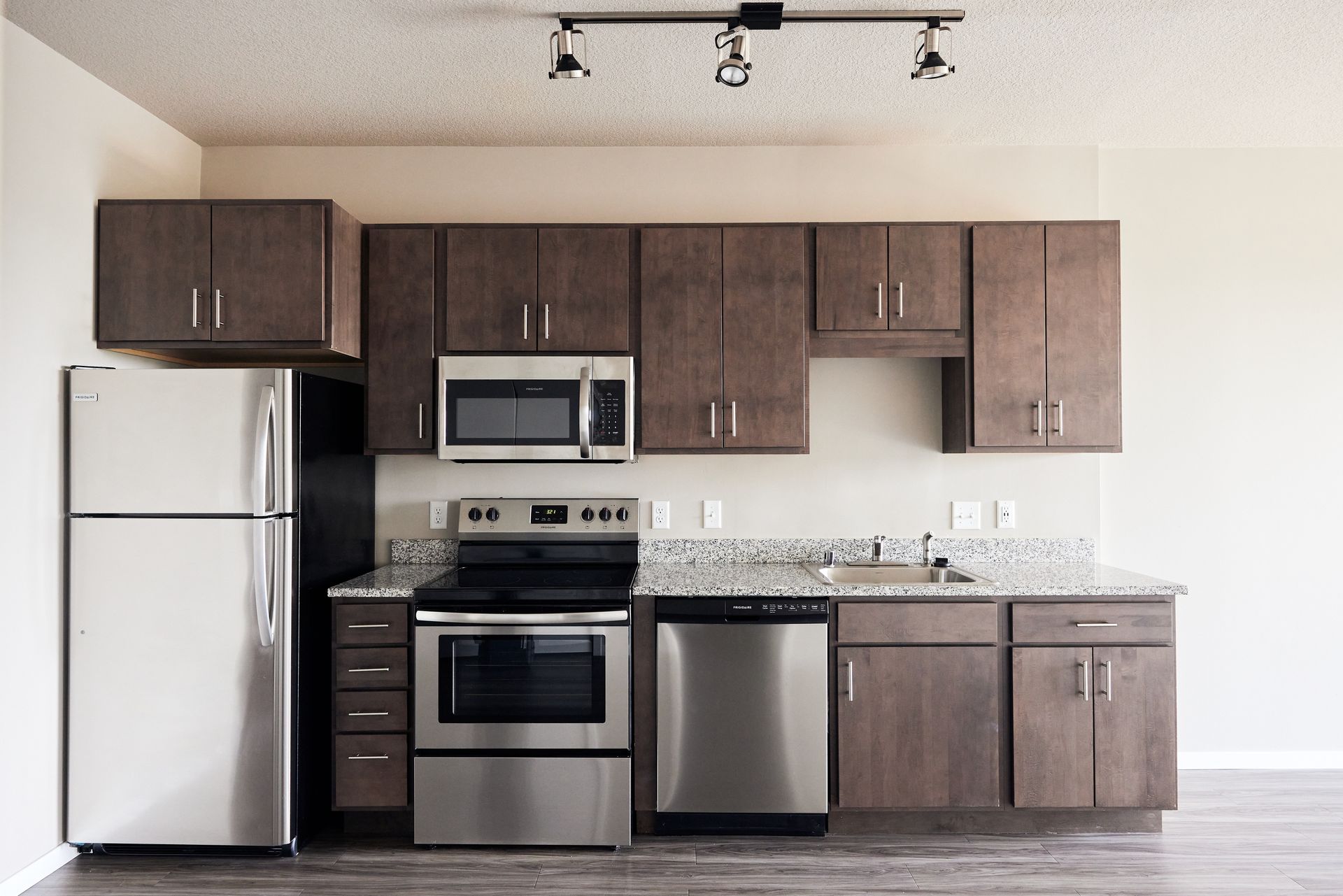 A modern kitchen with stainless steel appliances, brown cabinets, and a granite countertop.