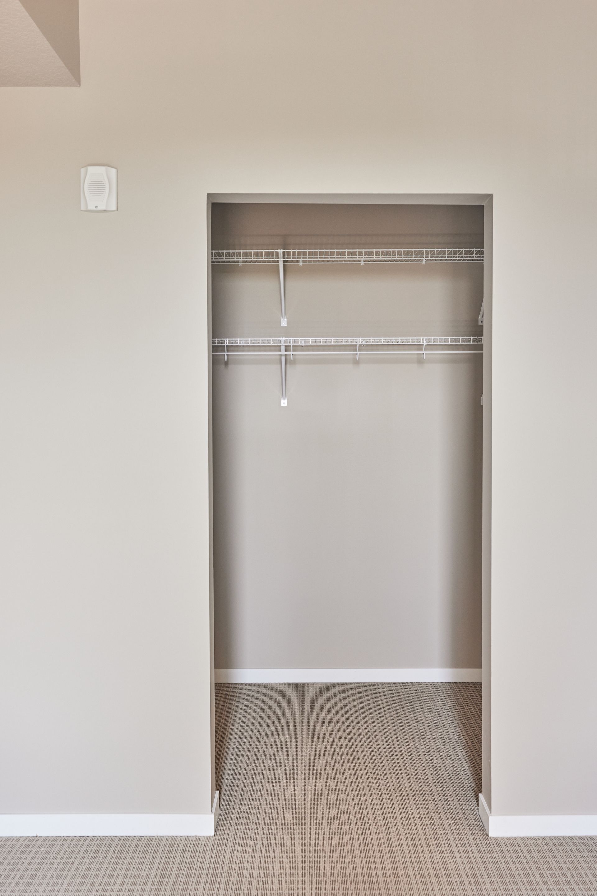 Empty walk-in closet with wire shelving and carpeted floor, beige walls.