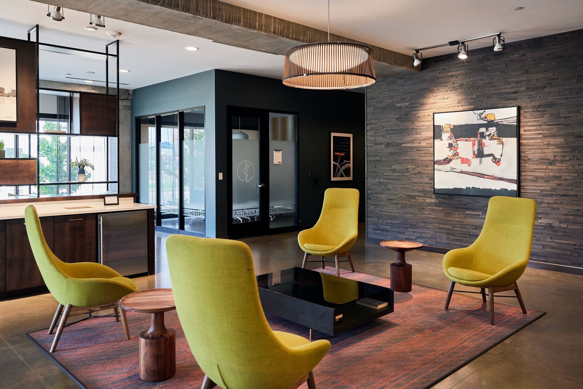 Lounge area with yellow chairs, a black coffee table, and abstract art on a gray brick wall.