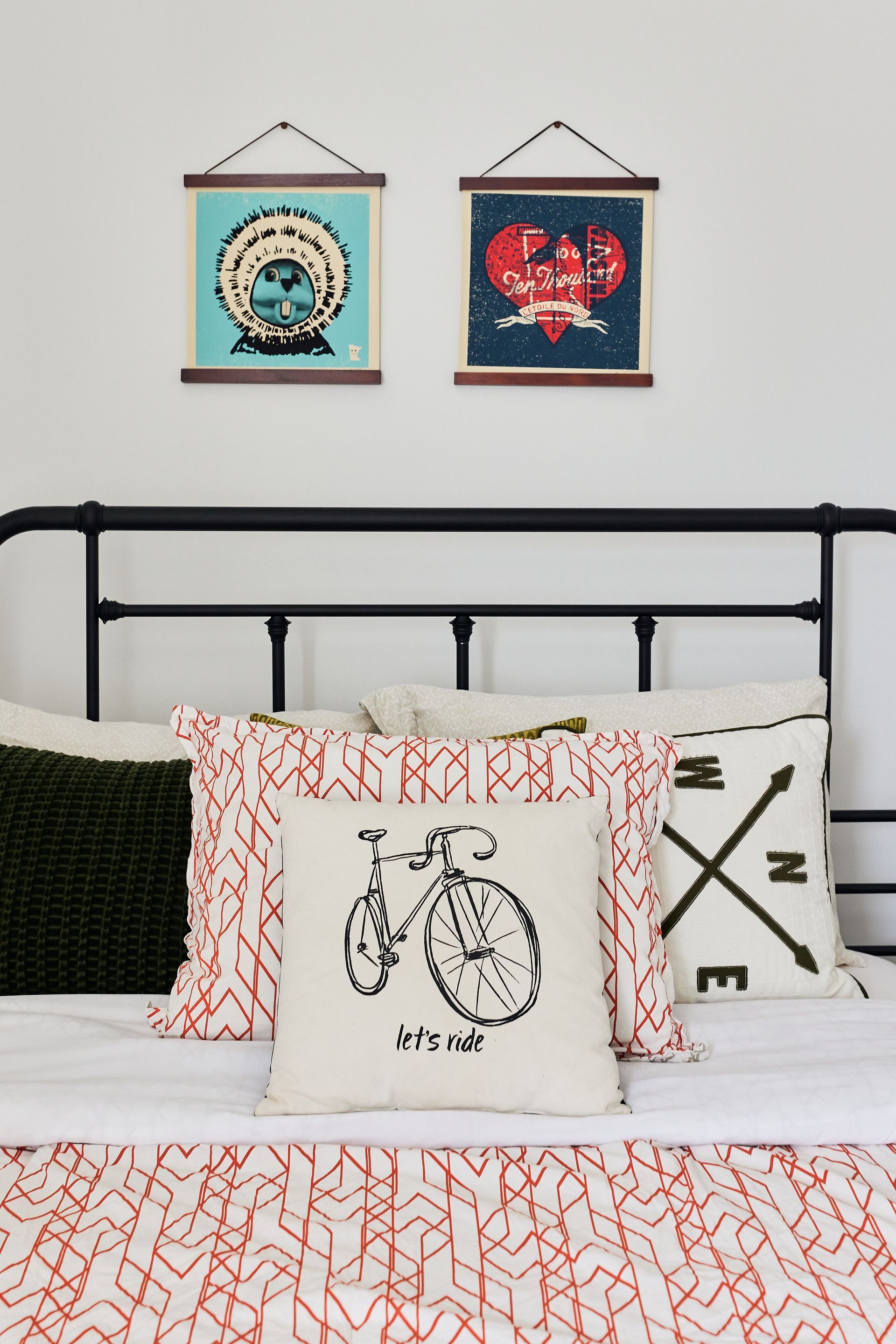 Bedroom with a black metal bed frame, decorative pillows, and two framed artworks above.