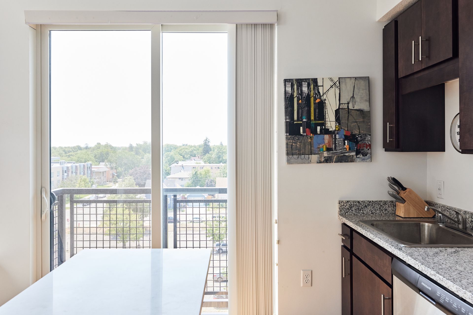Kitchen with balcony access and cityscape view. Features dark cabinets, artwork, and a white table.