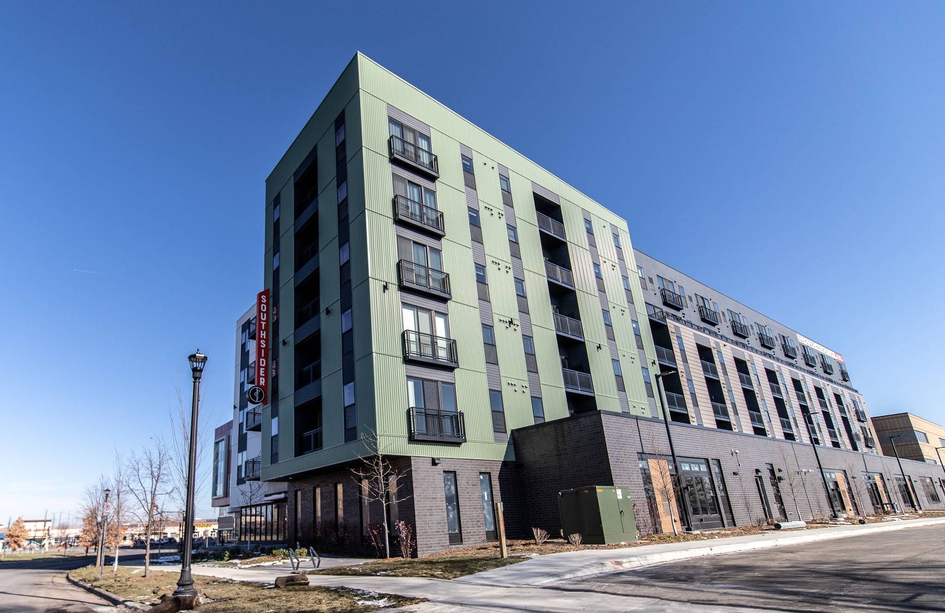 Multi-story modern building with green and black facade against a blue sky.