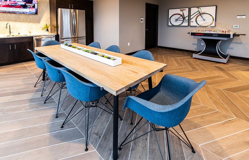 Long wooden table with blue chairs in a room with a foosball table and art.