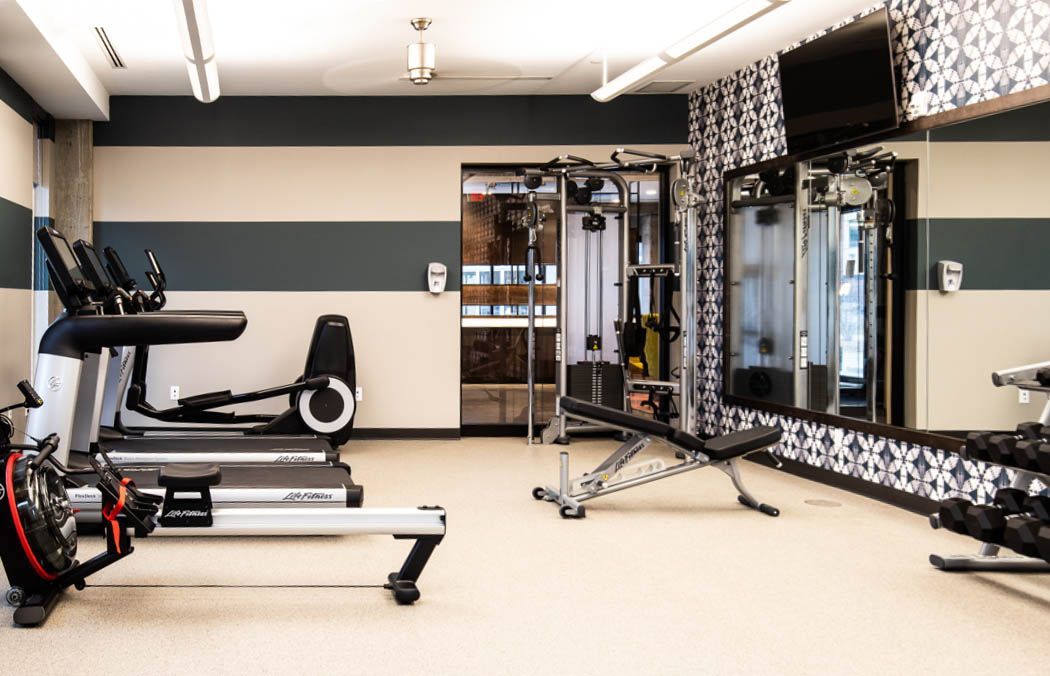 Gym interior with exercise equipment: treadmill, elliptical, rowing machine, weights.