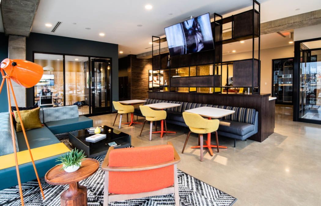 Modern lounge with seating, tables, tv, and orange accents; a social gathering space.