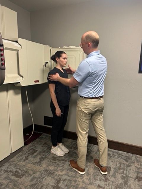 A professional assists a person standing at a medical imaging device for an X-ray in a clinic.