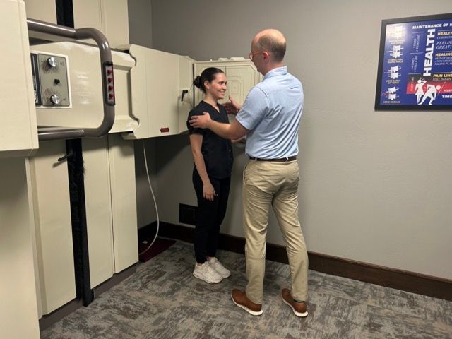 A professional instructs a patient on positioning for an X-ray in a clinical office setting.