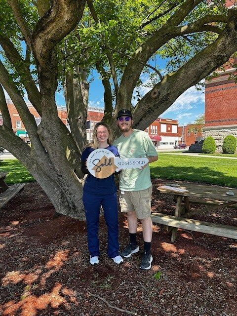 A man and a woman are standing in front of a tree holding signs.