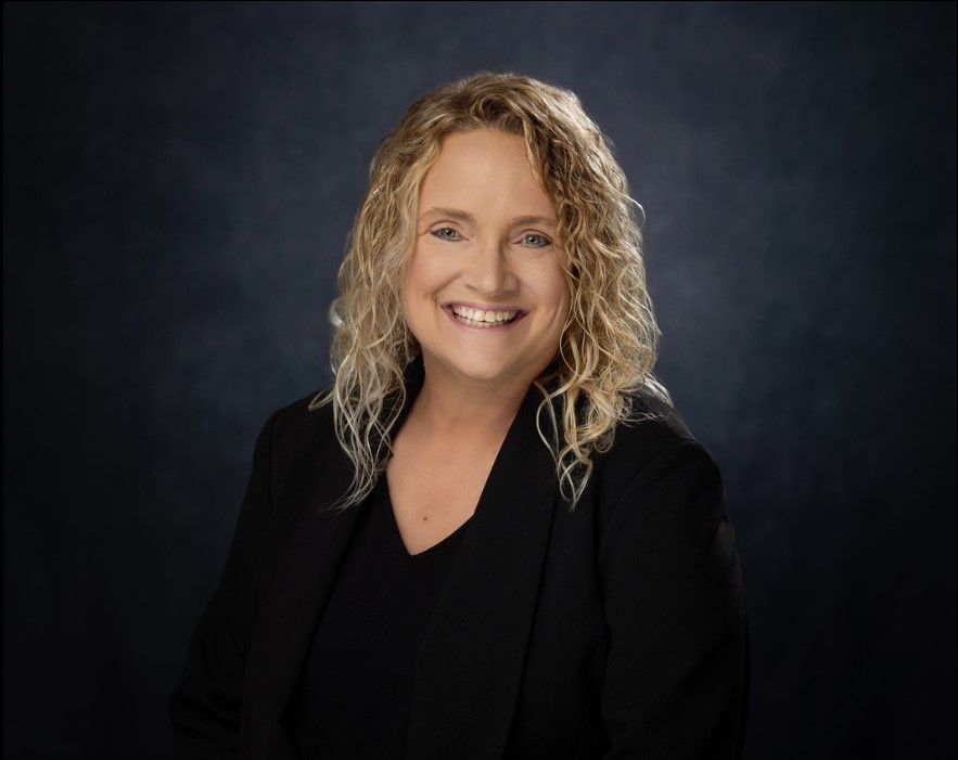 A woman with curly hair is smiling and wearing a black jacket.