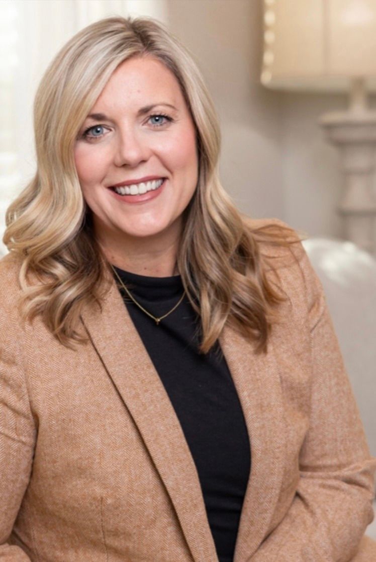 A woman wearing a tan jacket and a black shirt is smiling for the camera.