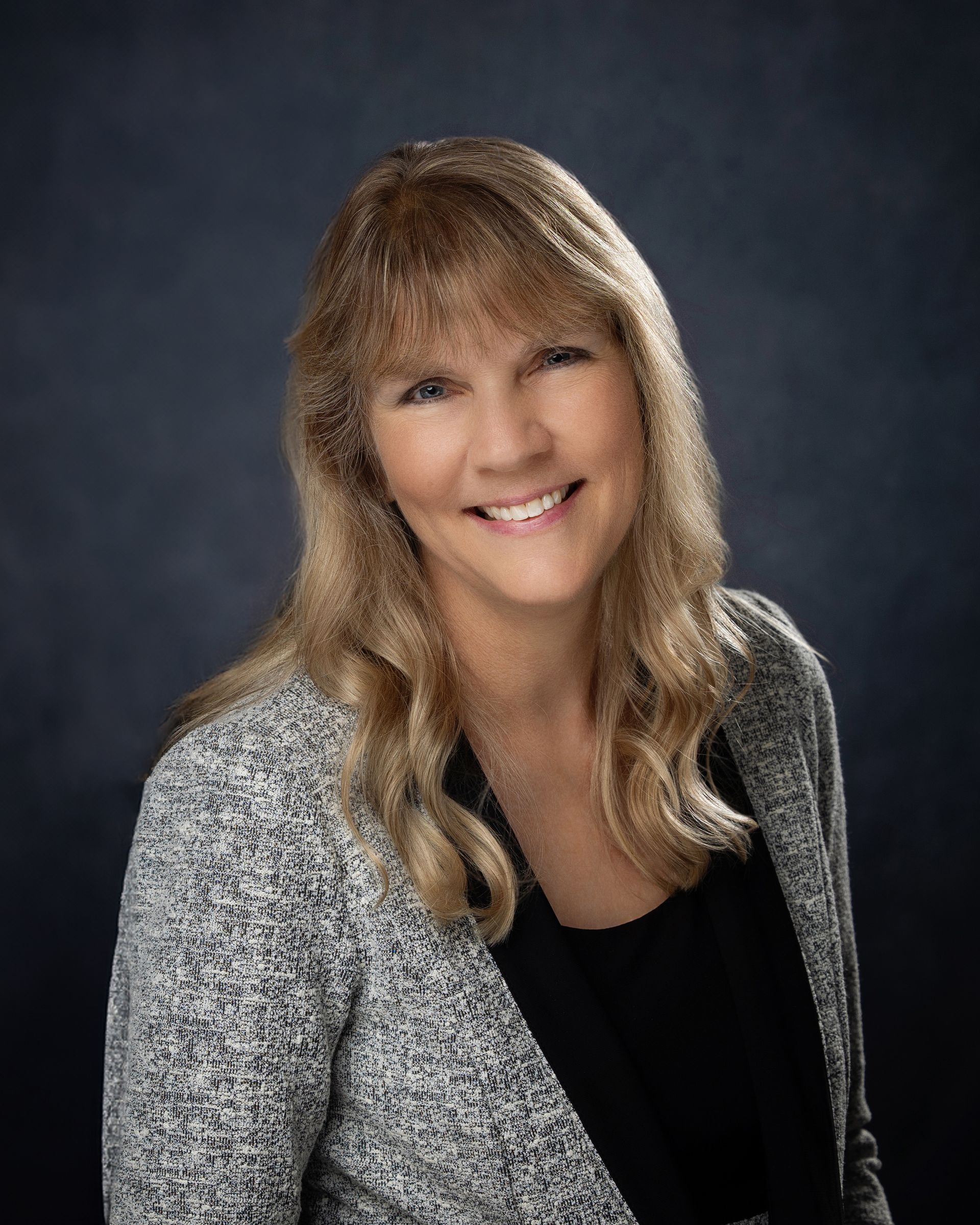 A woman in a gray jacket and black shirt is smiling for the camera.