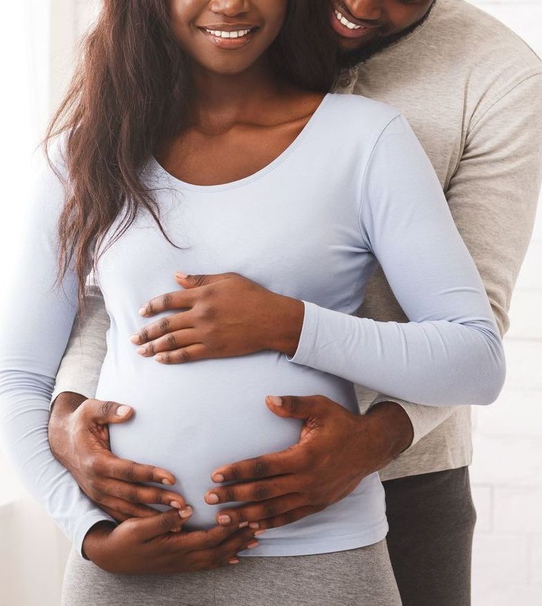 A man is hugging a pregnant woman in front of a window