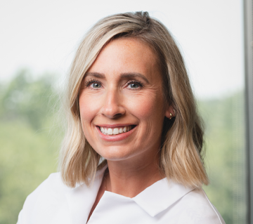 A woman in a white shirt is smiling in front of a window.