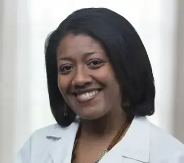 A woman in a white lab coat is smiling for the camera.