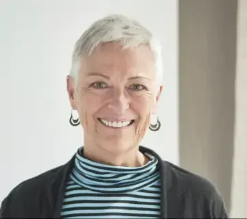 A woman wearing a striped turtleneck and earrings is smiling for the camera.