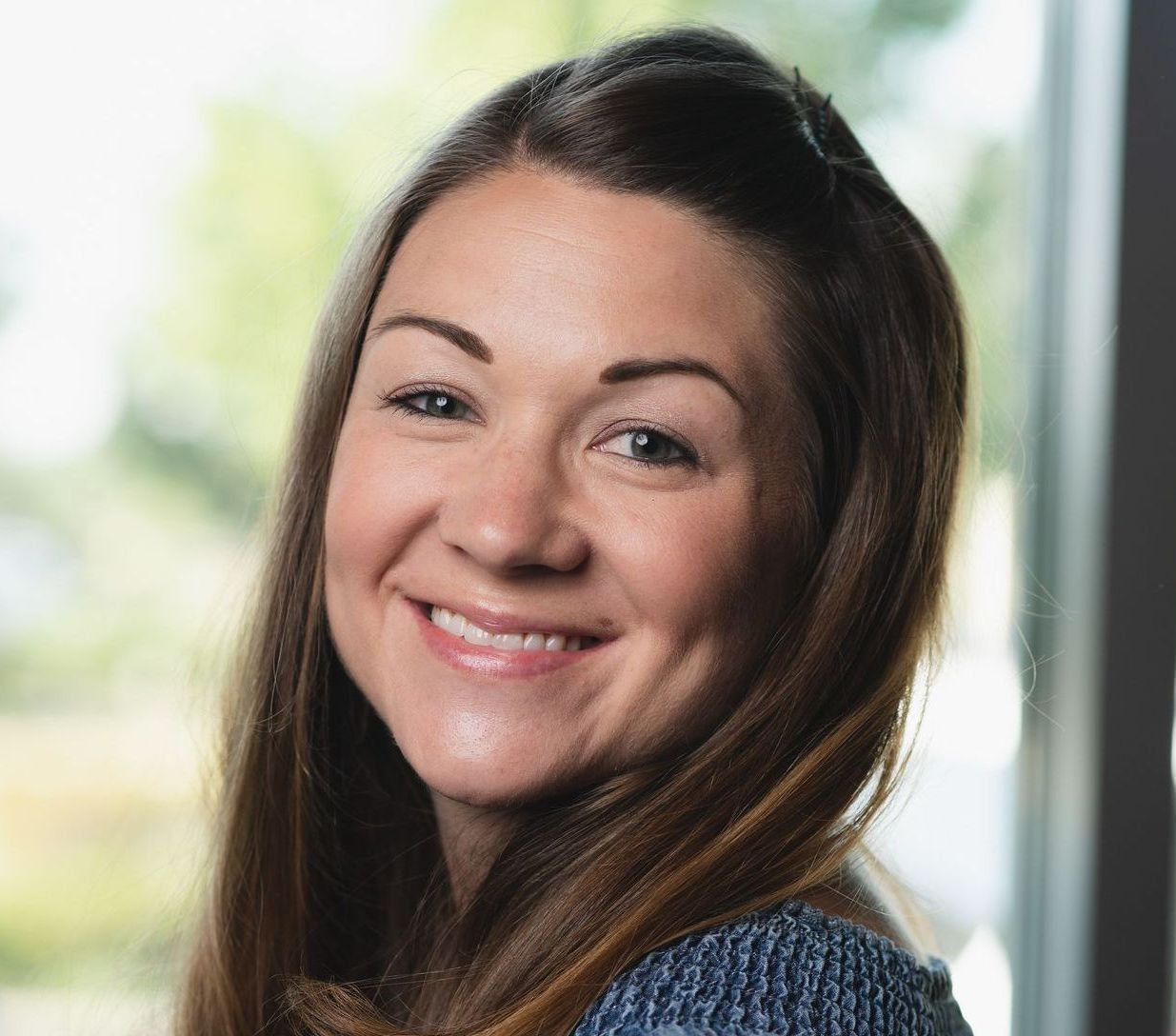 A woman is smiling for the camera in front of a window.