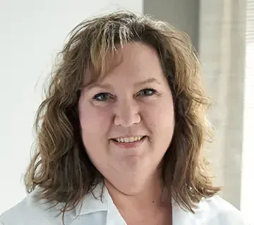 A woman in a white lab coat is smiling.