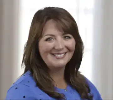 A woman in a blue shirt is smiling for the camera.