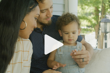 A man and woman are sitting on a porch with a baby.