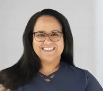 A woman wearing glasses and a blue shirt is smiling for the camera.