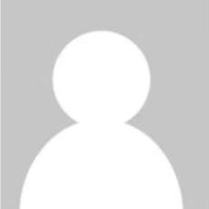 A couple smiles for a close-up photo, both wearing casual clothing, with an indoor dining setting in the background.