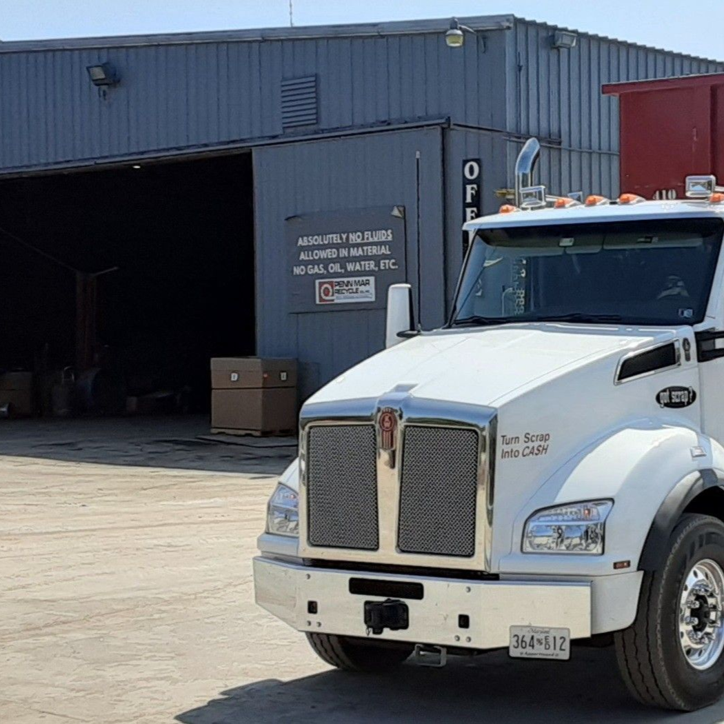 A white semi-truck parked in front of an industrial building with a sign on the wall.