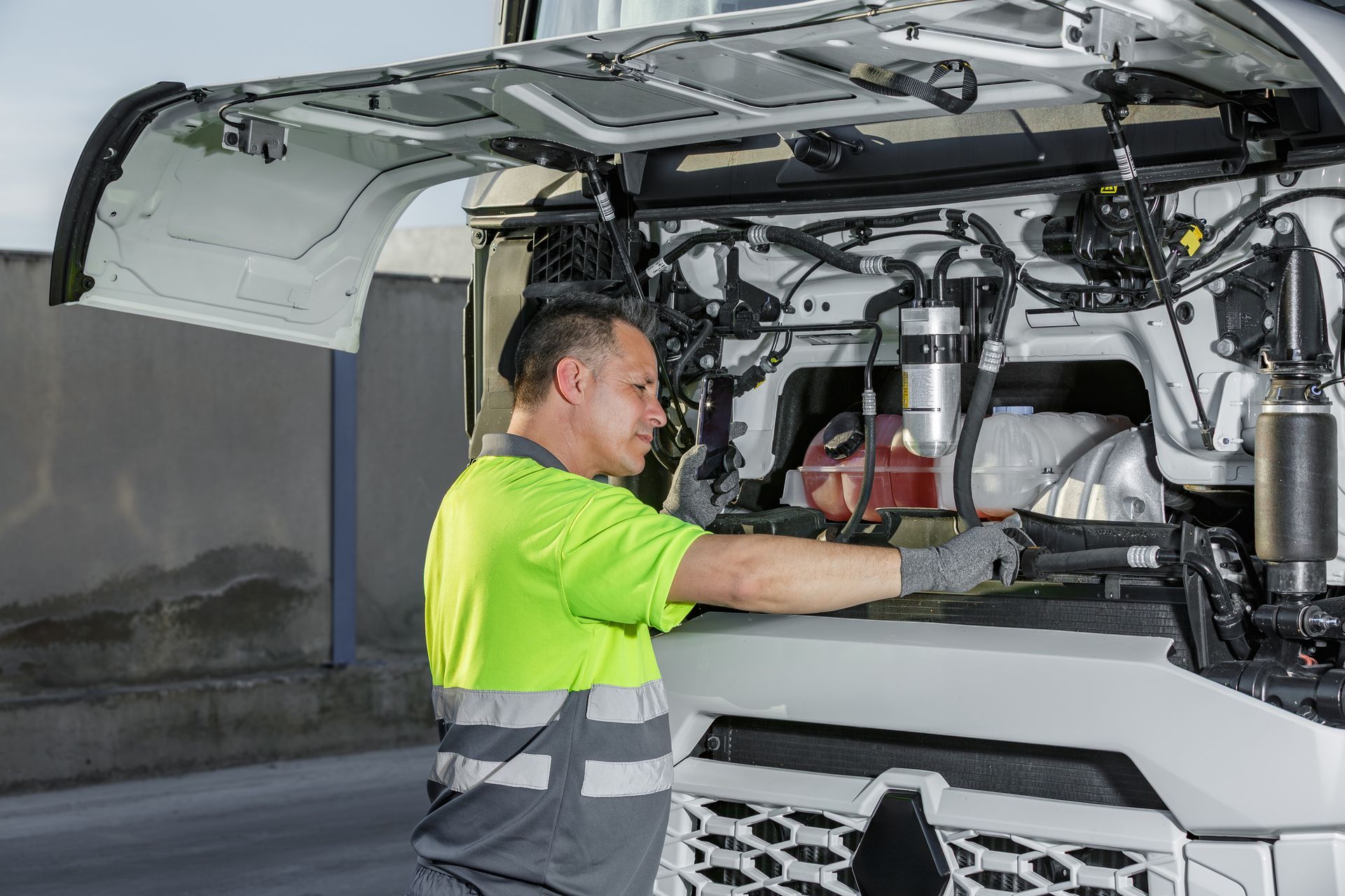 Mechanic using truck repair equipment to inspect engine under lifted hood of white semi-truck