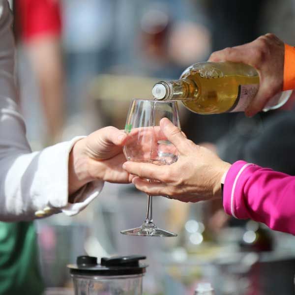Person pouring white wine into a glass, outdoors.
