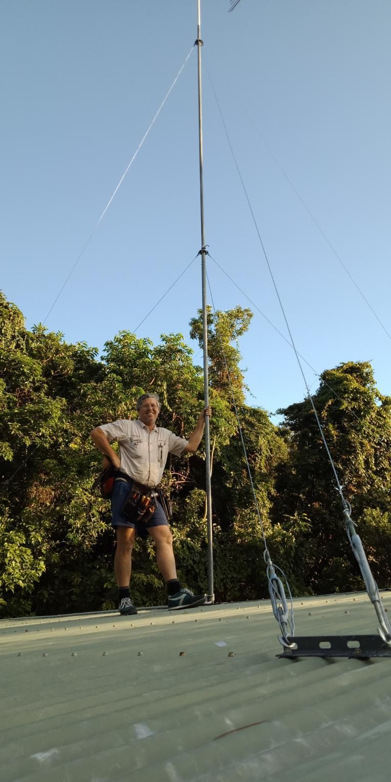 A Man Is Standing On Top Of A Roof Next To A Tall Pole — Laurence Capocchi Antenna Guy In Trinity Beach, QLD