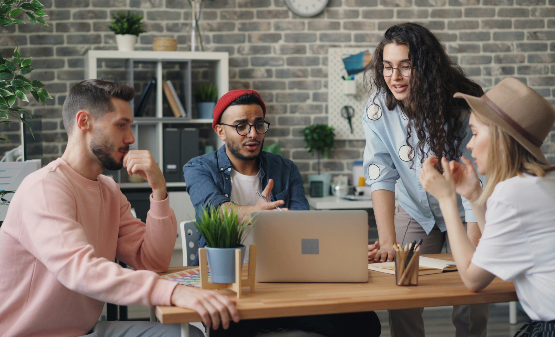 Person writing in notebook and typing on laptop at a desk with a sticky note.