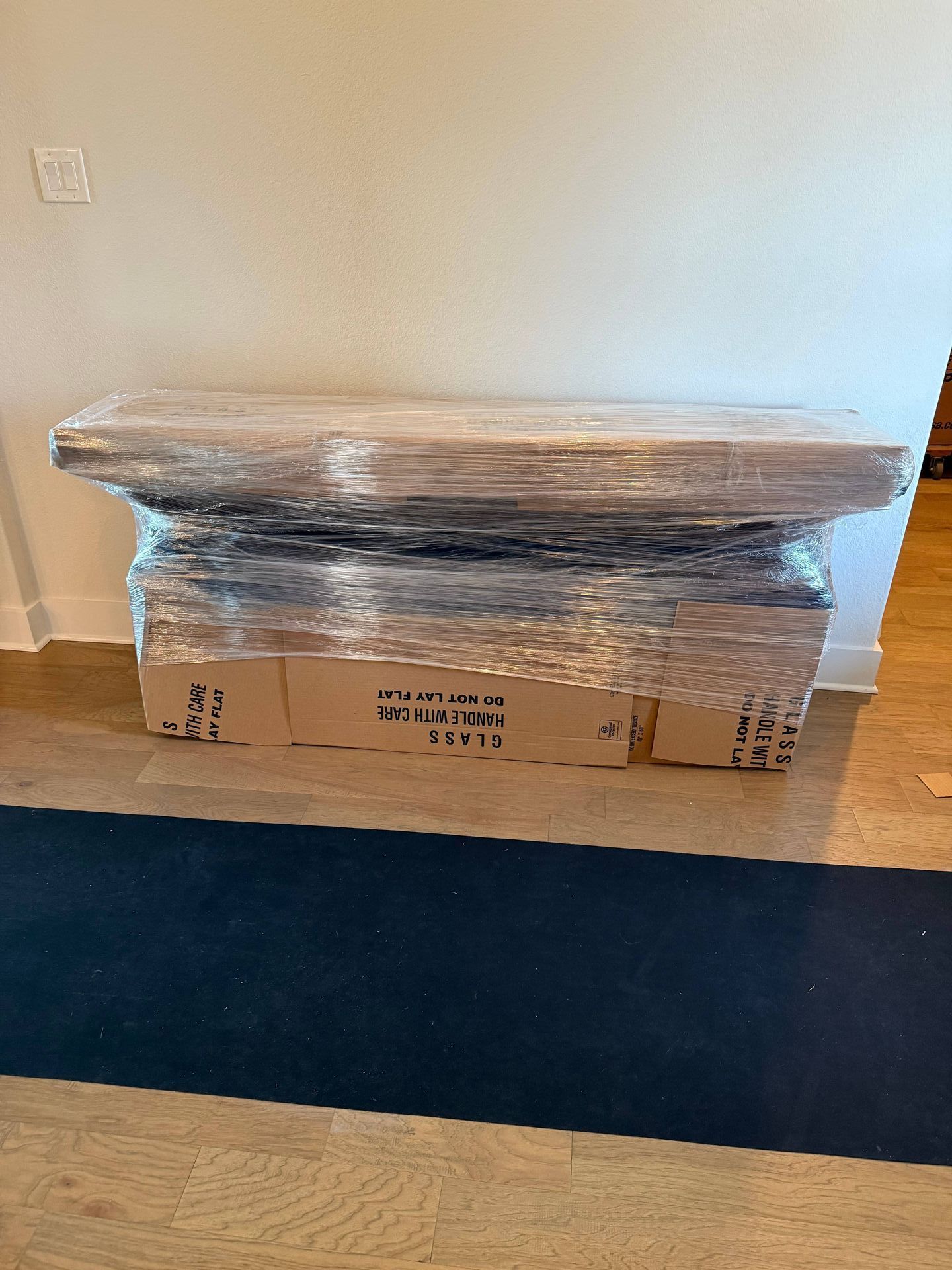 A wooden table is wrapped in plastic wrap in a living room.