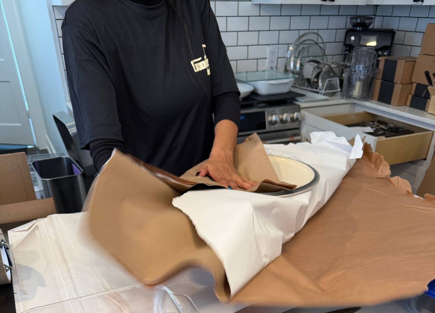 A woman is wrapping a bowl in brown paper in a kitchen
