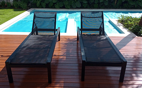 Duas espreguiçadeiras estão sobre um deck de madeira ao lado de uma piscina.
