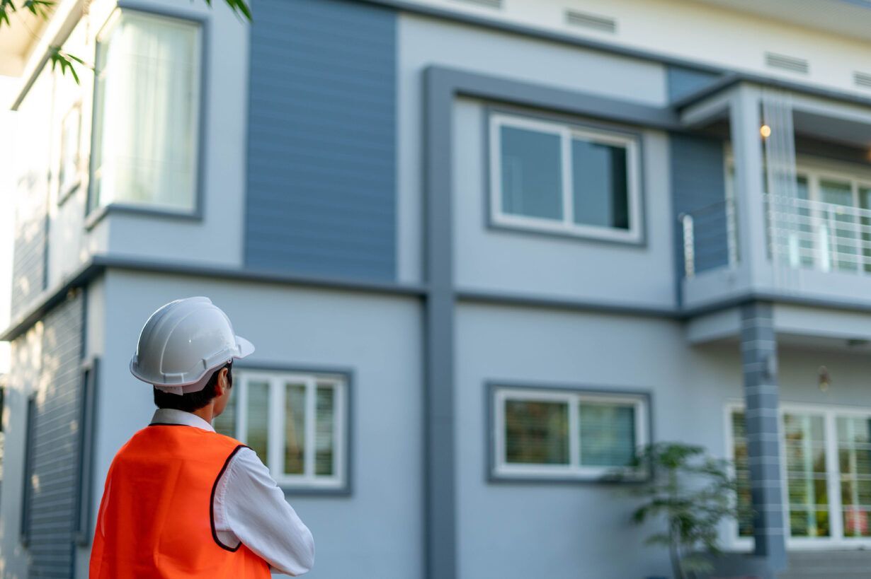 A Man in an Orange Vest and Hard Hat is Standing in Front of a Large House — Vale Building Inspections in Bateau Bay, NSW
