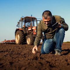 A man is kneeling down in a field with a tractor in the background.