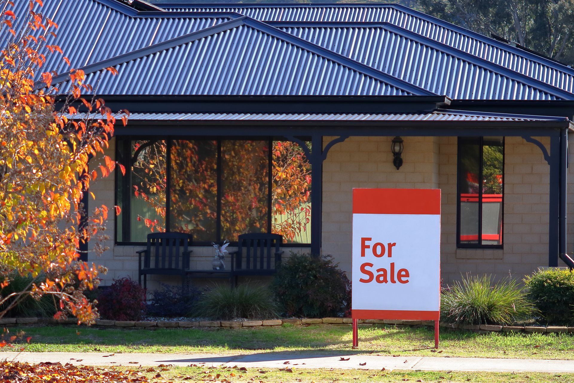 For sale sign in front of a blue house; three people stand on the porch.