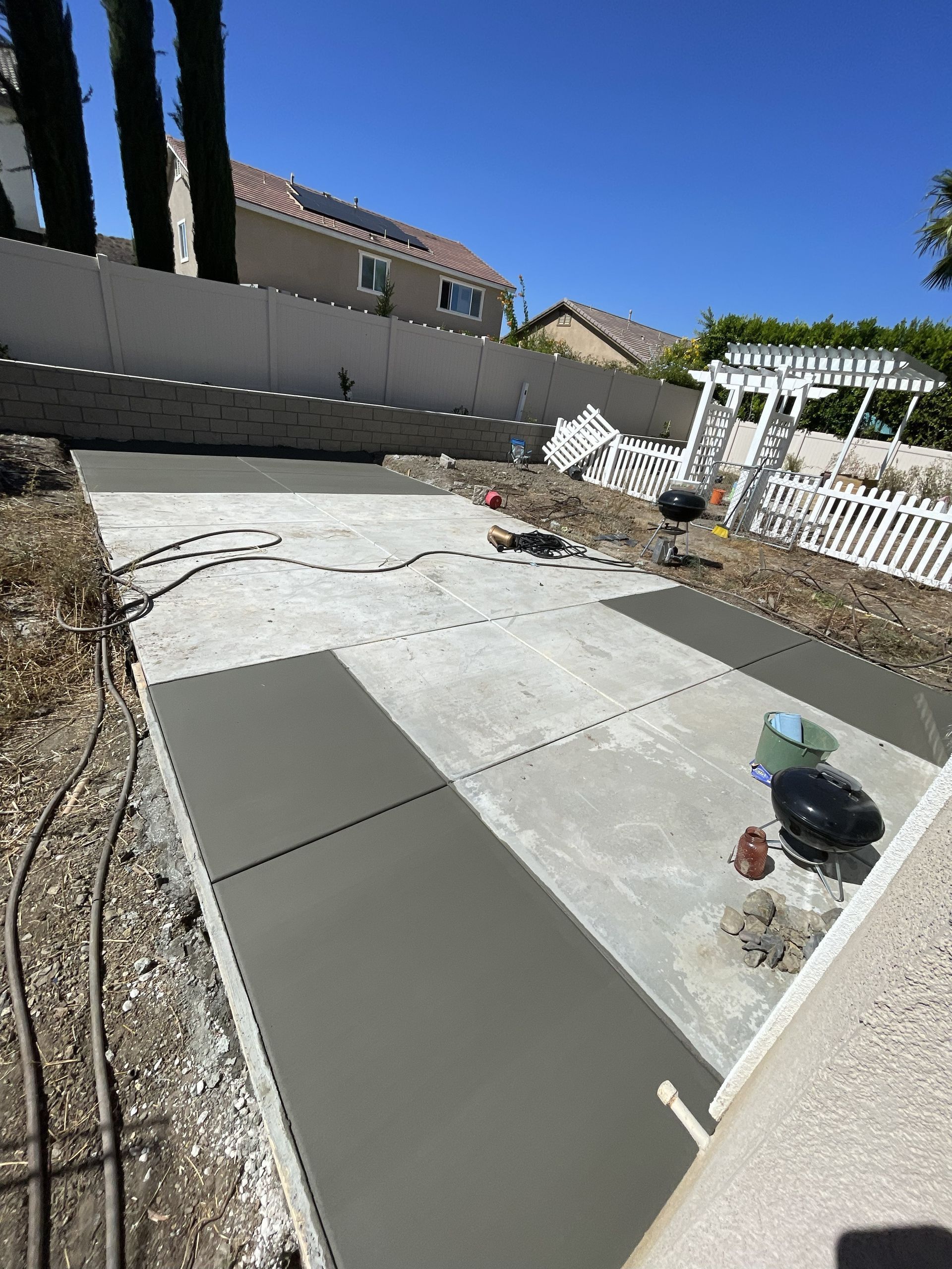 Concrete patio construction in a backyard, with forms in place and a partially poured section.