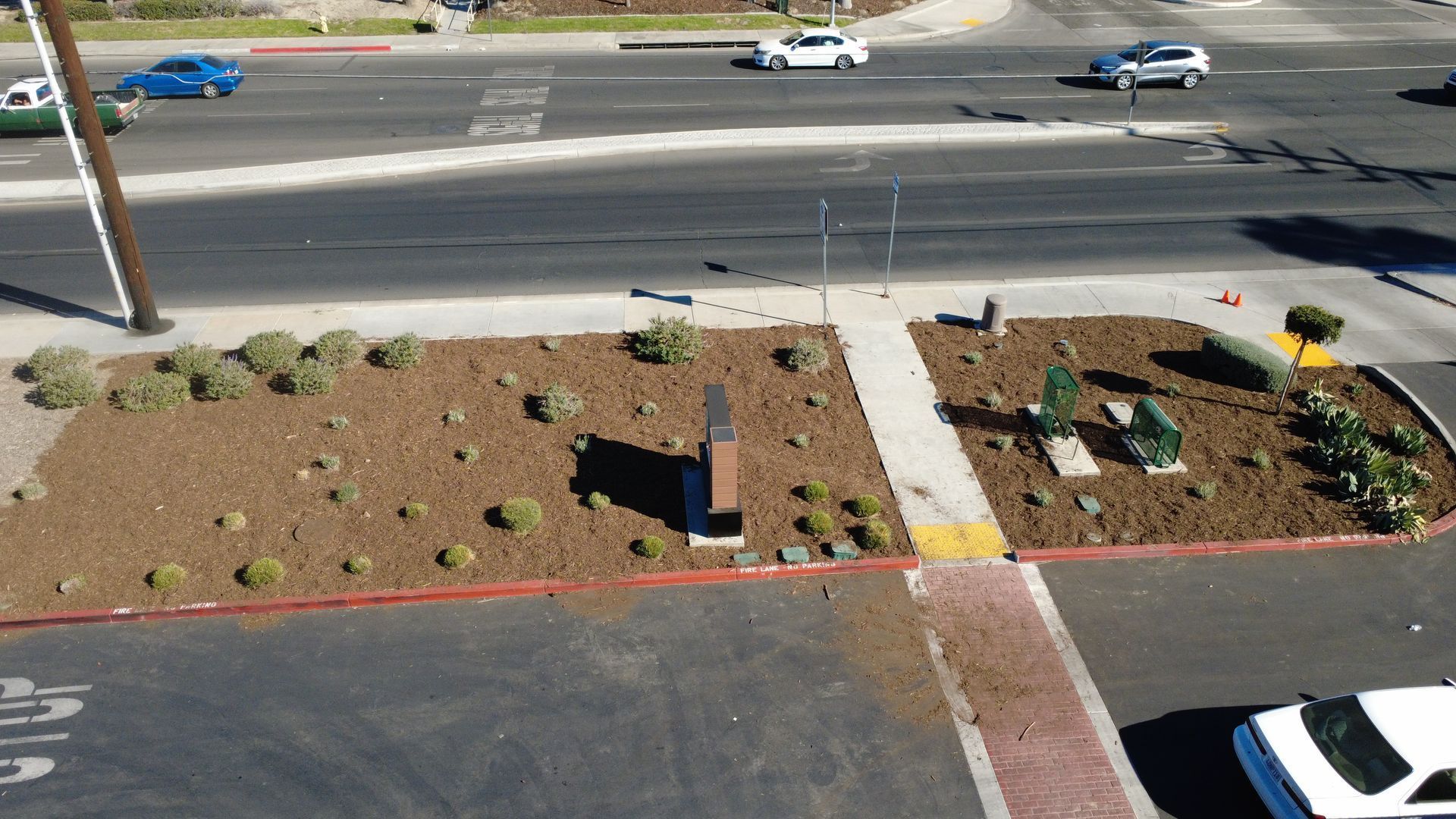 Street scene with cars on a multi-lane road, pedestrian island with landscaping, and a sidewalk.